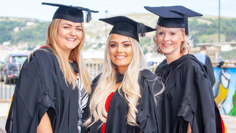 Three higher education learners celebrating on graduation day