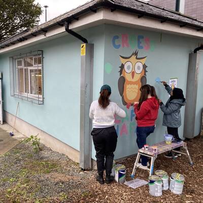 Students painting a mural on the wall of Caffi Hafan in Bangor