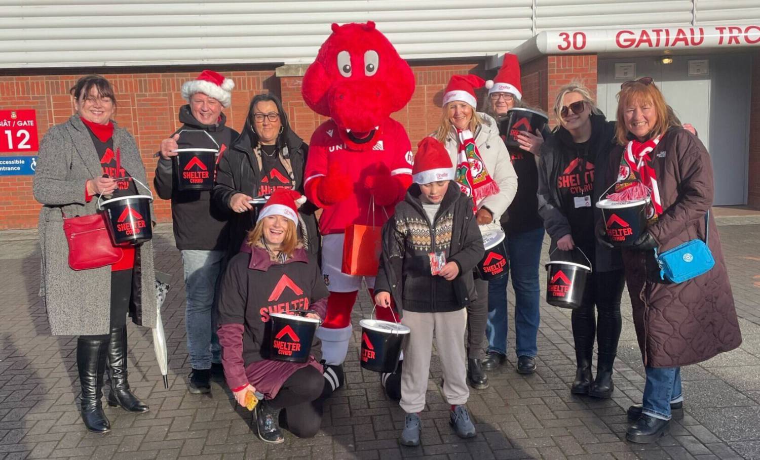 Shelter Cymru volunteers with Rex the Dragon outside The Racecourse Ground in Wrexham