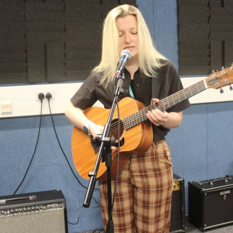 Hannah Popey singing and playing guitar in a recording studio at Coleg Llandrillo