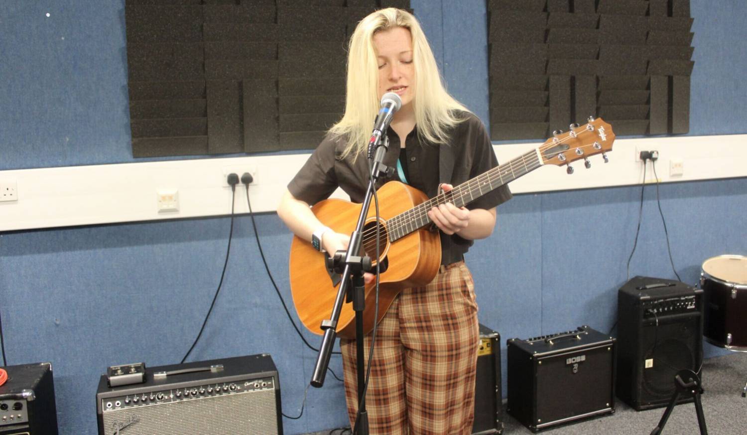 Hannah Popey singing and playing guitar in a recording studio at Coleg Llandrillo