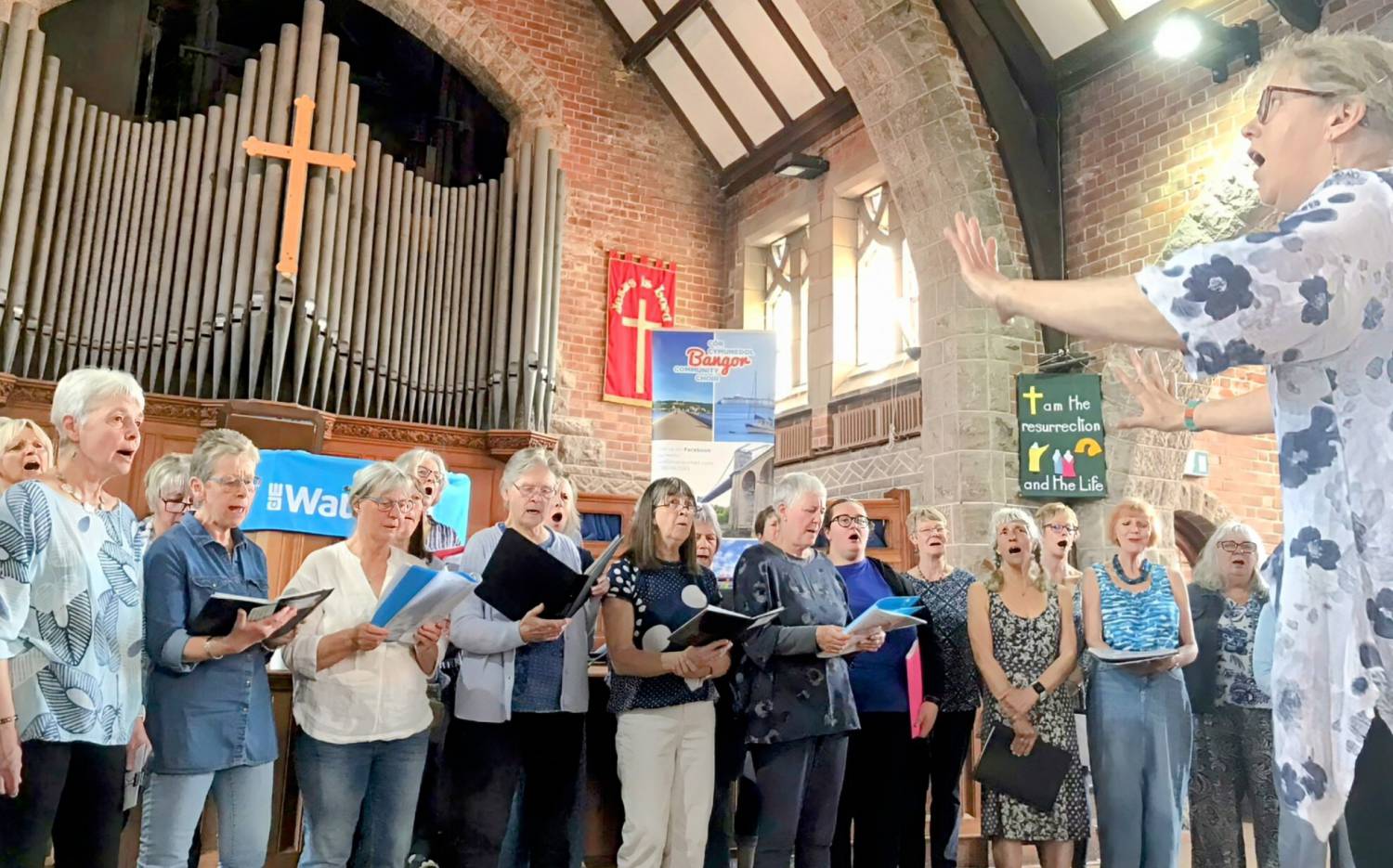 Sara Brown yn arwain côr Coastal Voices a Chôr Cymunedol Bangor yn Eglwys Ddiwygiedig Unedig Llandrillo-yn-Rhos