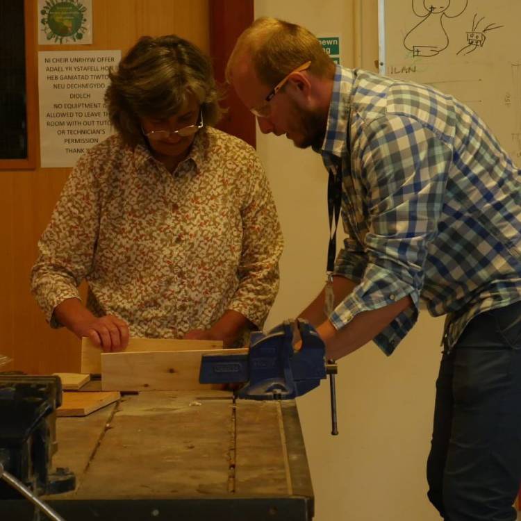 Jakub, y tiwtor, yn helpu dysgwr rhaglen Lluosi yn ystod cwrs Sgiliau Gwaith Coed a Rhifedd Ymarferol