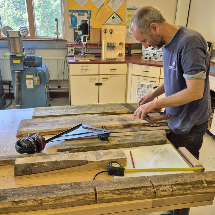 Jamie Walker, dysgwr ar y rhaglen Lluosi, yn mesur pren i wneud bwrdd coffi yn ystod cwrs Sgiliau Gwaith Coed a Rhifedd Ymarferol