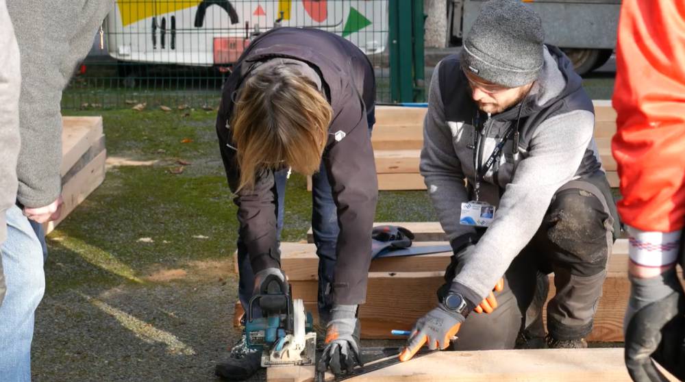 Y tiwtor Lluosi Jakub Gawel yn helpu dysgwr yn ystod dosbarth gwaith coed yn hwb cymunedol Porthi Dre yng Nghaernarfon