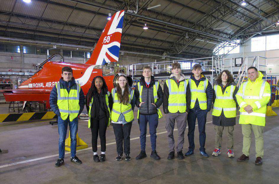 Coleg Menai students in a hangar at Babcock International, RAF Valley, with a Red Arrows Hawk T1 aircraft in the background