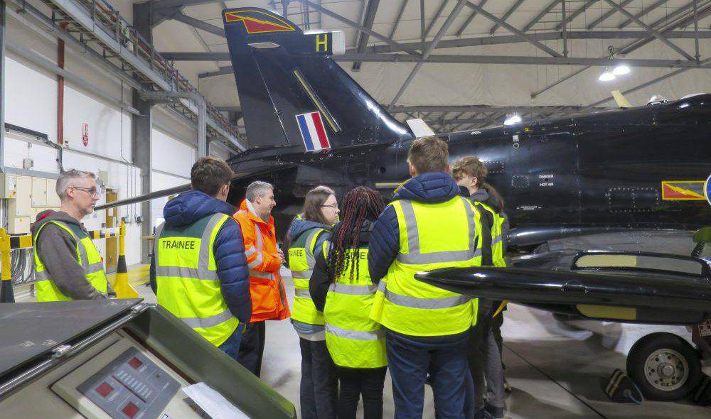 Coleg Menai students talking to a Babcock engineer while looking at a Hawk T2 aircraft at Babcock International, RAF Valley
