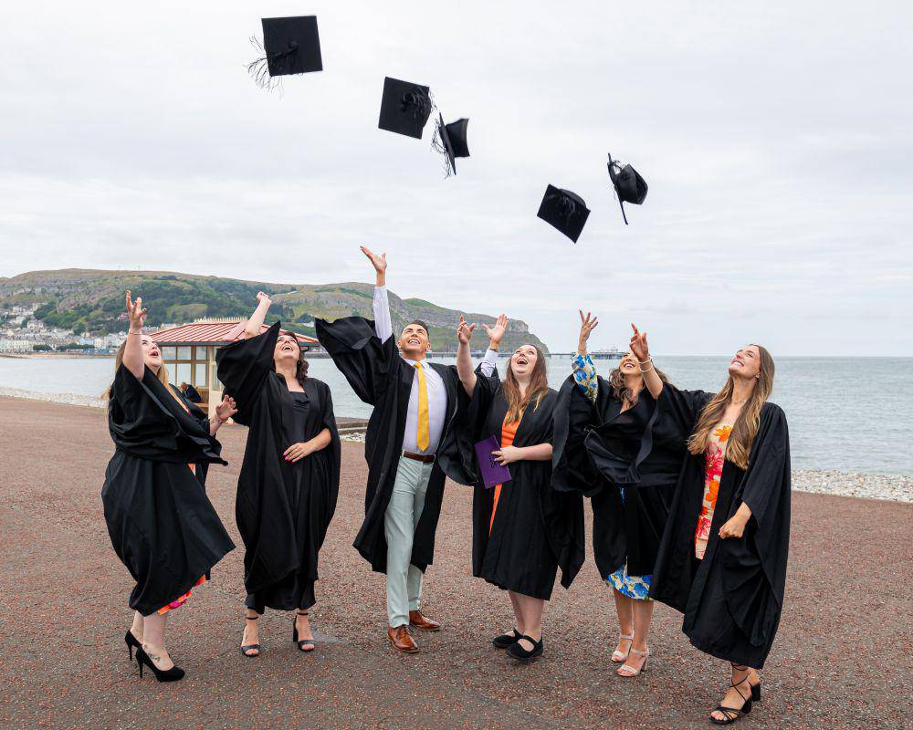 Myfyrwyr yn dathlu graddio ar y promenâd yn Llandudno
