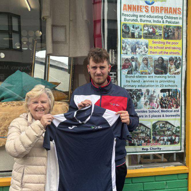 Coleg Menai staff member Jamie Jones presenting Reverend Pauline Edwards with a football kit outside the Annie’s Orphans shop in Bangor