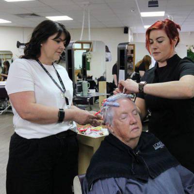 Michelle Jones (chwith) yn goruchwylio myfyrwraig yn steilio gwallt cwsmer yn y salon ar gampws Coleg Llandrillo yn Llandrillo-yn-Rhos