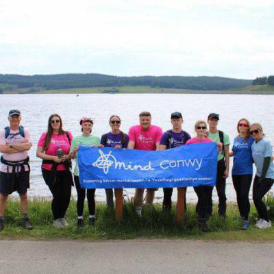 Myfyrwyr, darlithwyr a staff Mind Conwy gyda baner Mind Conwy ger Llyn Brenig