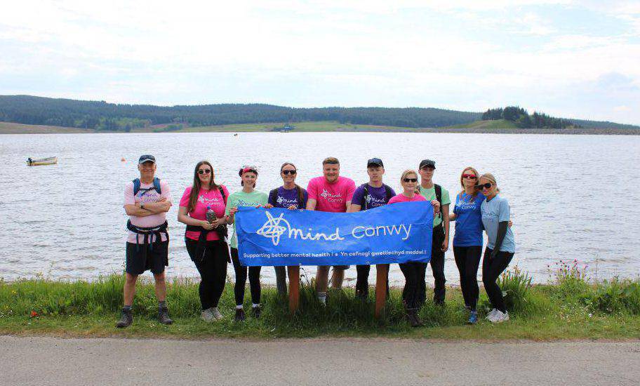 Students, lecturers and Conwy Mind staff holding a Mind Conwy banner at Llyn Brenig
