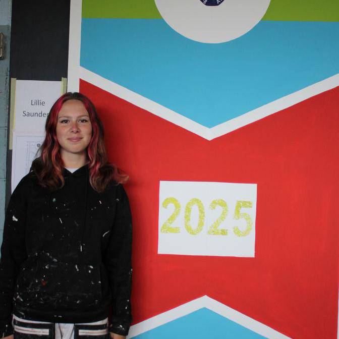 Lillie Saunders o flaen y wal a baentiodd i ennill rownd ranbarthol cystadleuaeth Prentis Paentio ac Addurno'r Flwyddyn
