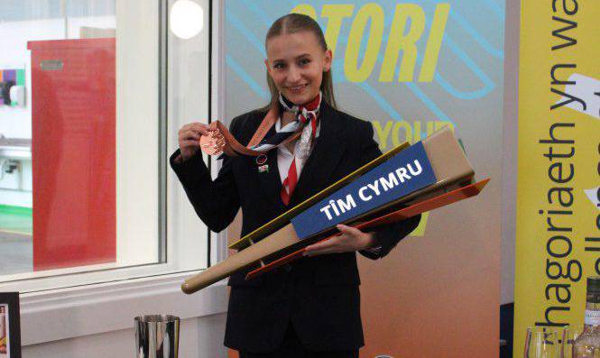 Myfyriwr lletygarwch o Goleg Llandrillo, Yuliia Batrak, yn dal fflam Tîm Cymru a'i Medal am Ragoriaeth yn EuroSkills