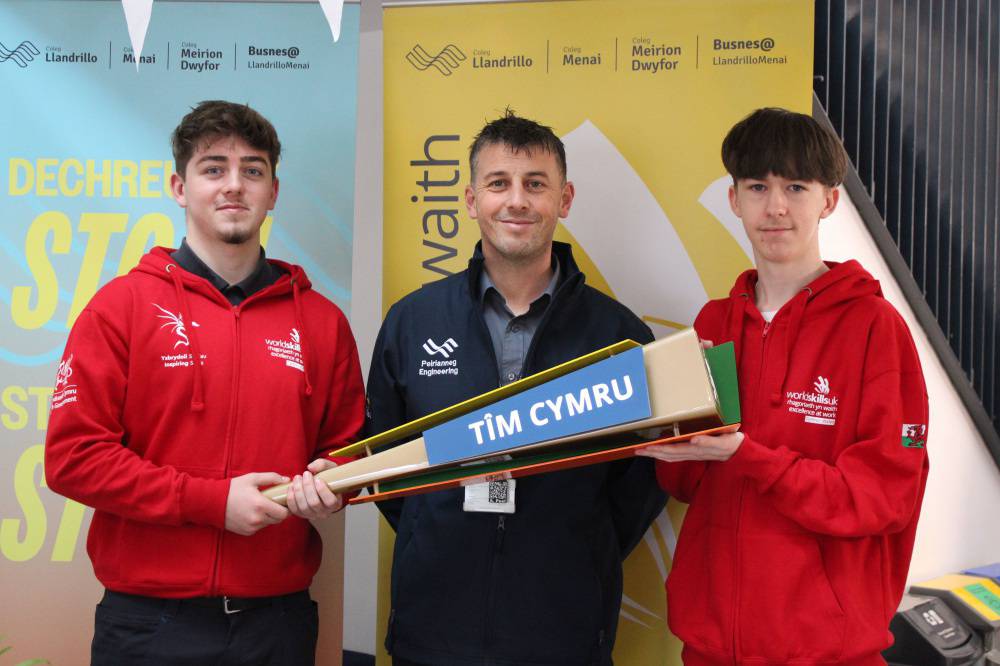 McKenzie Goodwin-Cotterill a Zack Arnold, myfyrwyr yn adran beirianneg Coleg Llandrillo'n dal fflam Tîm Cymru gyda'r darlithydd Arron Peel