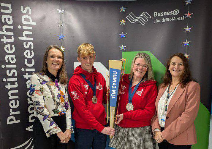 Tomos Jones a Lowri Hughes, prentisiaid Cyfrifyddu, yn dal fflam Tîm Cymru ⁠gyda staff Grŵp Llandrillo Menai