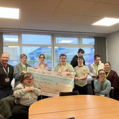 The students from the college are standing with representatives from Crest. They are holding a large cheque.