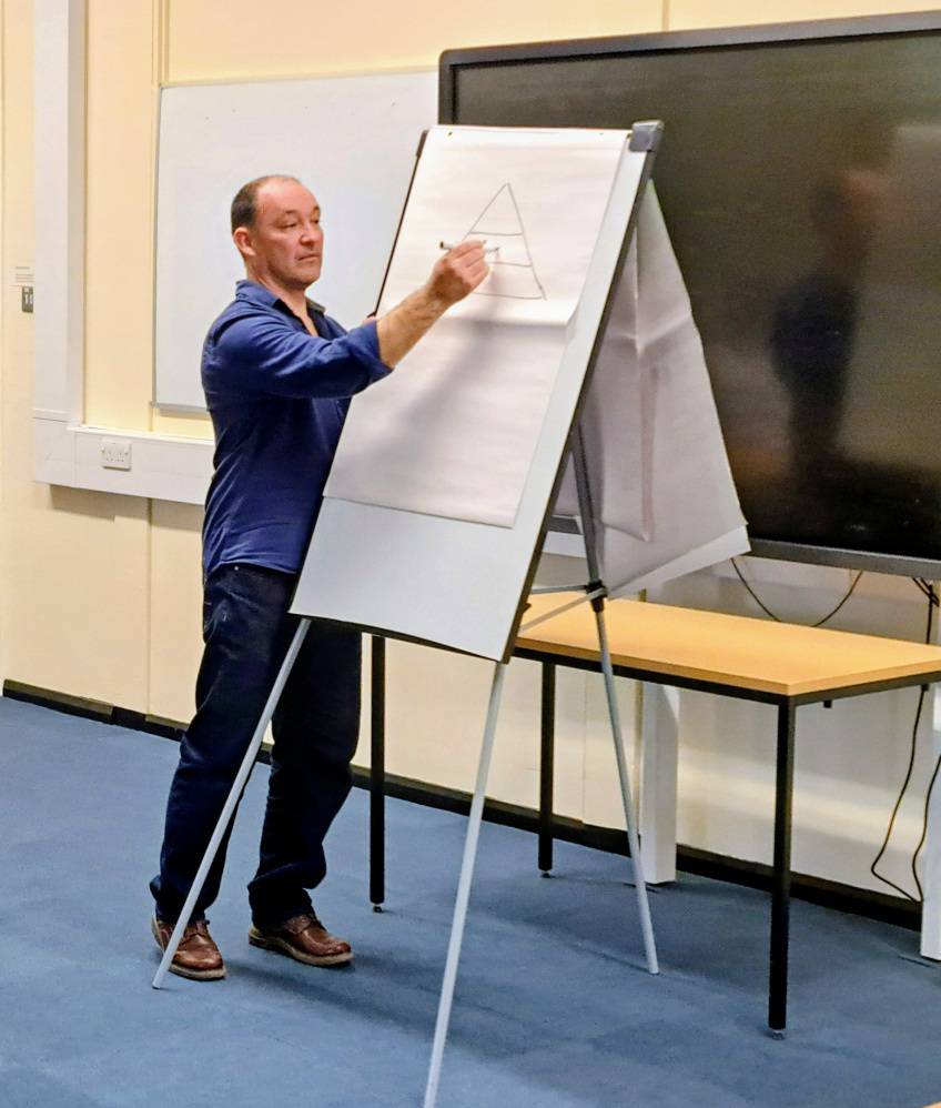 Yr awdur, Cynan Jones yn sefyll o flaen dosbarth yn ysgrifennu ar ddarn mawr o bapur.