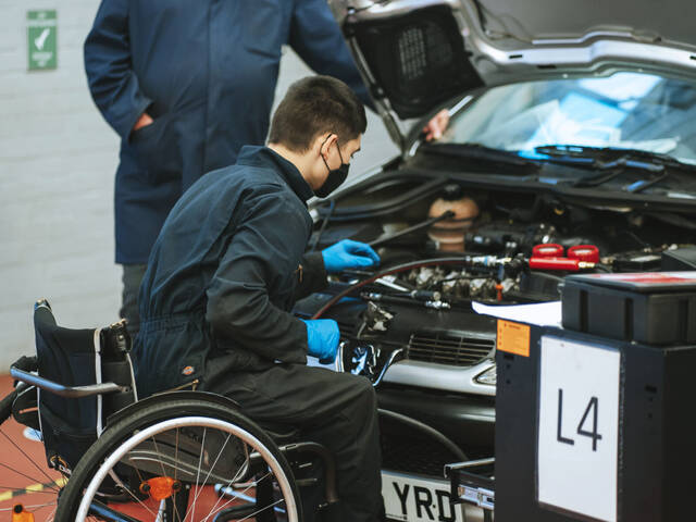 Wheelchaired learner fixing car engine